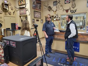 Dirk Turner showing Michael Roberts a gun safe alarm clock during his interview at Liberty T&T Safes. Producer, Emily Craw, is behind the camera capturing the action